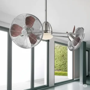 A modern dual ceiling fan with a brushed nickel finish and two rotating caged fan heads, installed in a bright room with large windows.